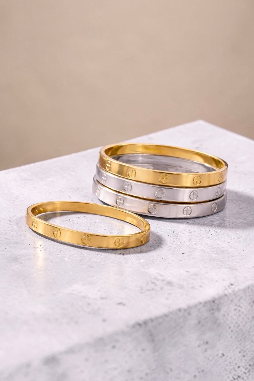 Gold and silver bangles on a marble surface with a beige background