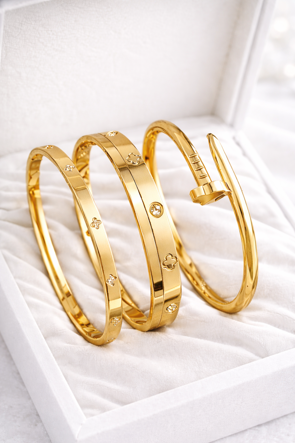 Three gold bangles with embedded stones on a white textured surface