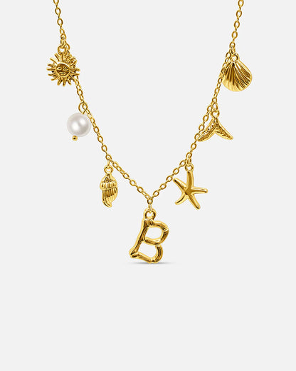 Gold necklace with various charms including a pearl, sun, shell, starfish, and letter 'B' on a white background.