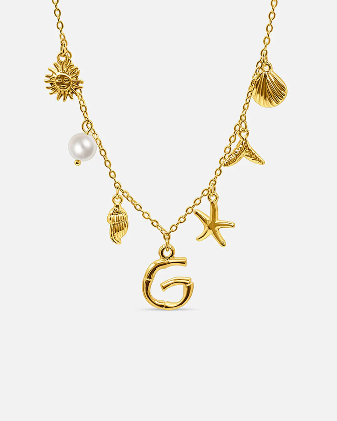 Gold necklace with various charms including a sun, shell, pearl, and letter 'G' on a white background.