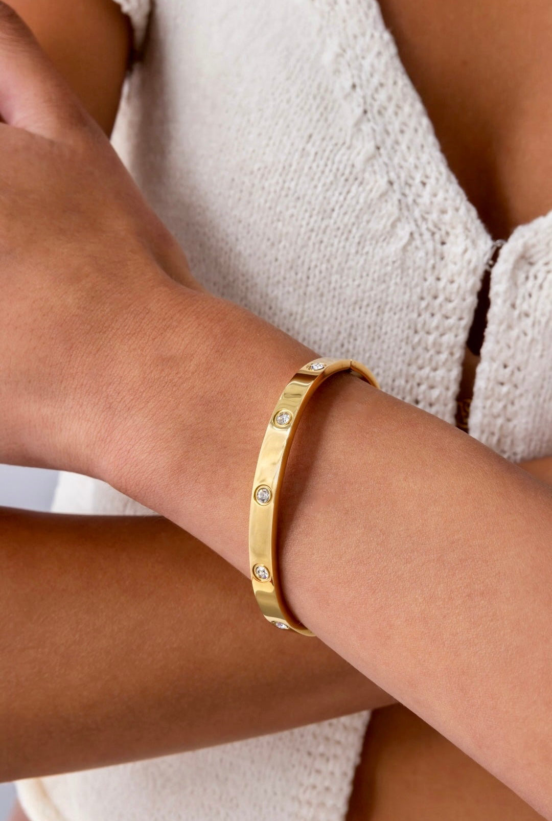 Gold bracelet with small stones on a wrist against a neutral background