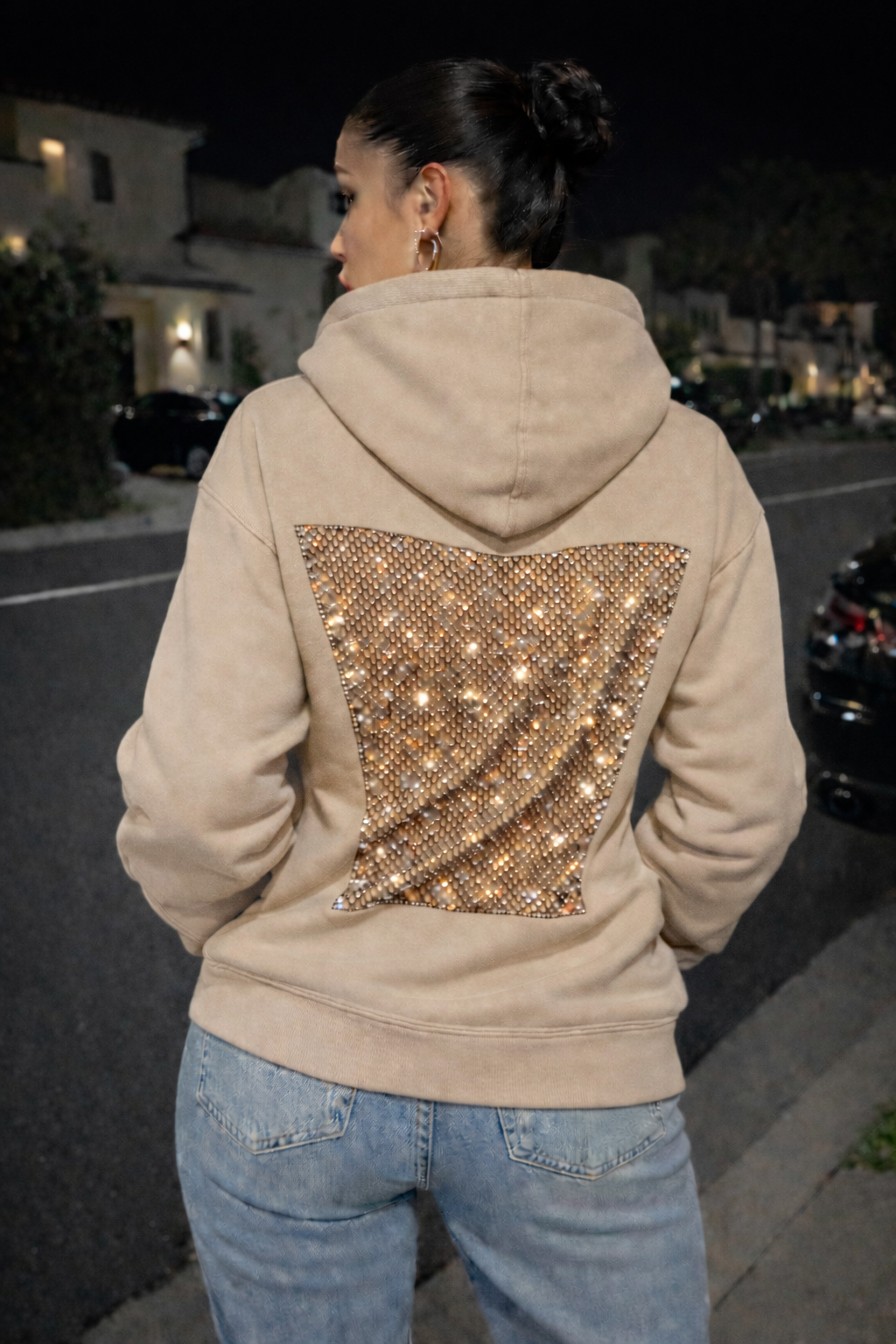 Person wearing a beige hoodie with a sequined back panel at night.