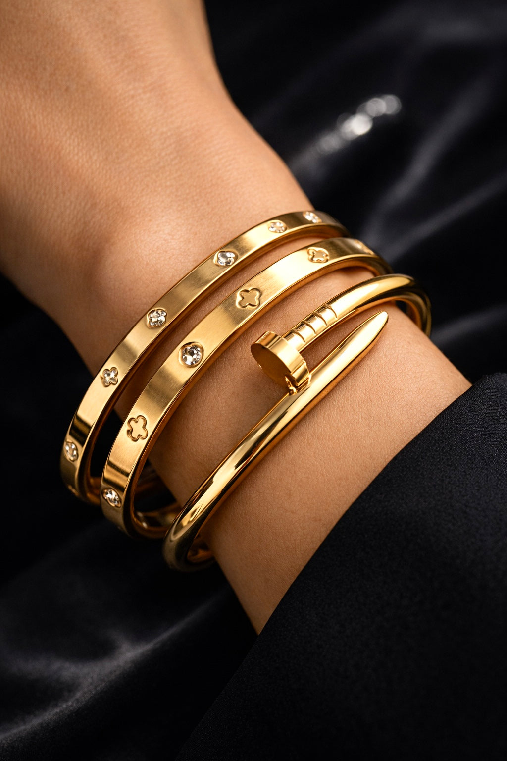 Gold bracelets with gemstones on a wrist against a black satin background