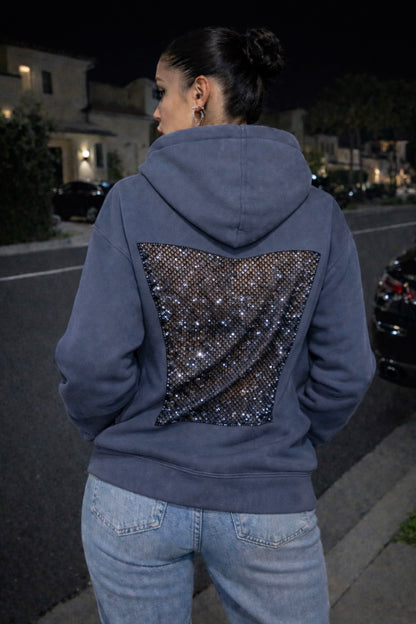 Person wearing a blue hoodie with a sparkling back design on a street at night.
