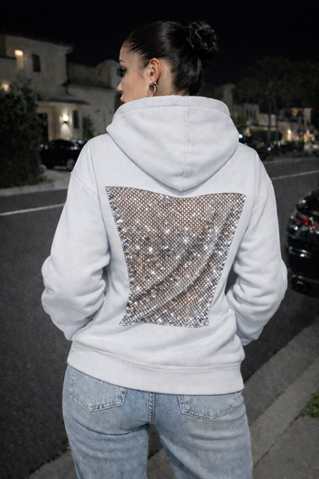 Person wearing a white hoodie with a sequin back design on a street at night.