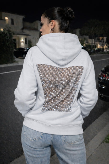 Person wearing a white hoodie with a sequin back design on a street at night.