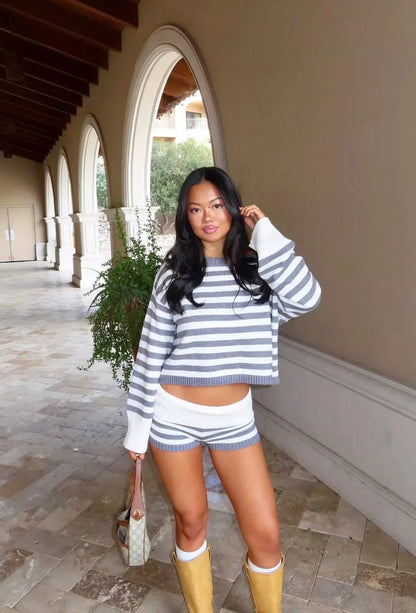 Woman in a striped sweater and shorts standing on a stone patio with arches in the background