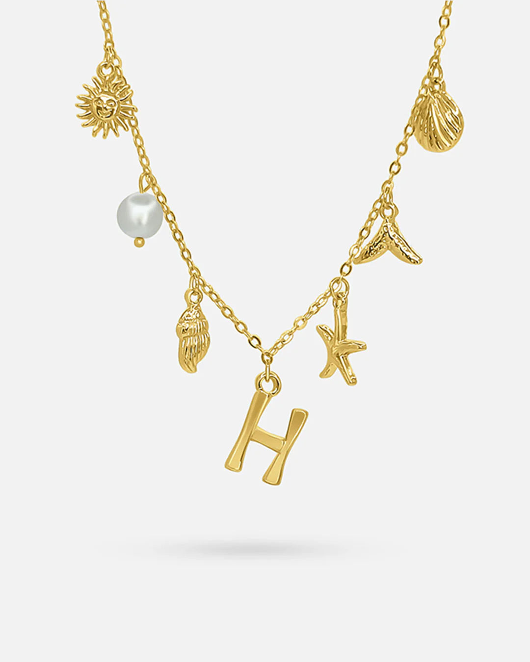 Gold necklace with various charms including a sun, shell, pearl, and letter 'H' on a white background.