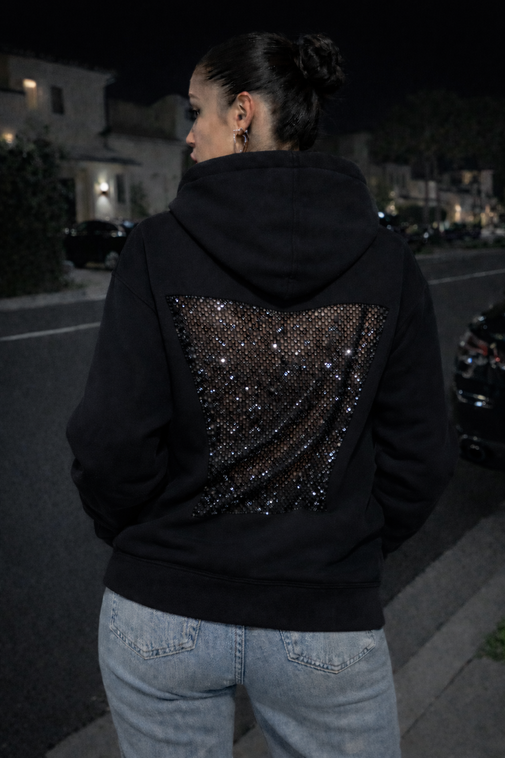 Person wearing a black hoodie with sequin details at night.