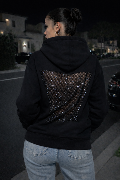 Person wearing a black hoodie with sequin details at night.