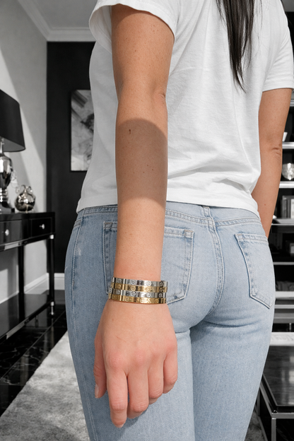Person wearing light blue jeans and a white shirt with a gold bracelet on a neutral background