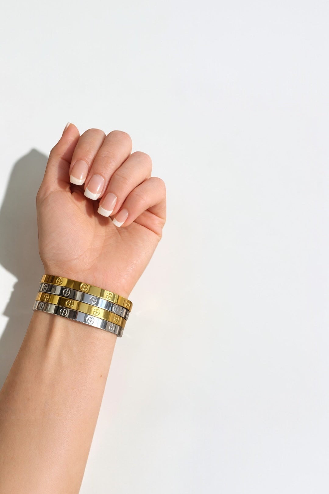 Hand wearing a stack of metallic bracelets on a light background