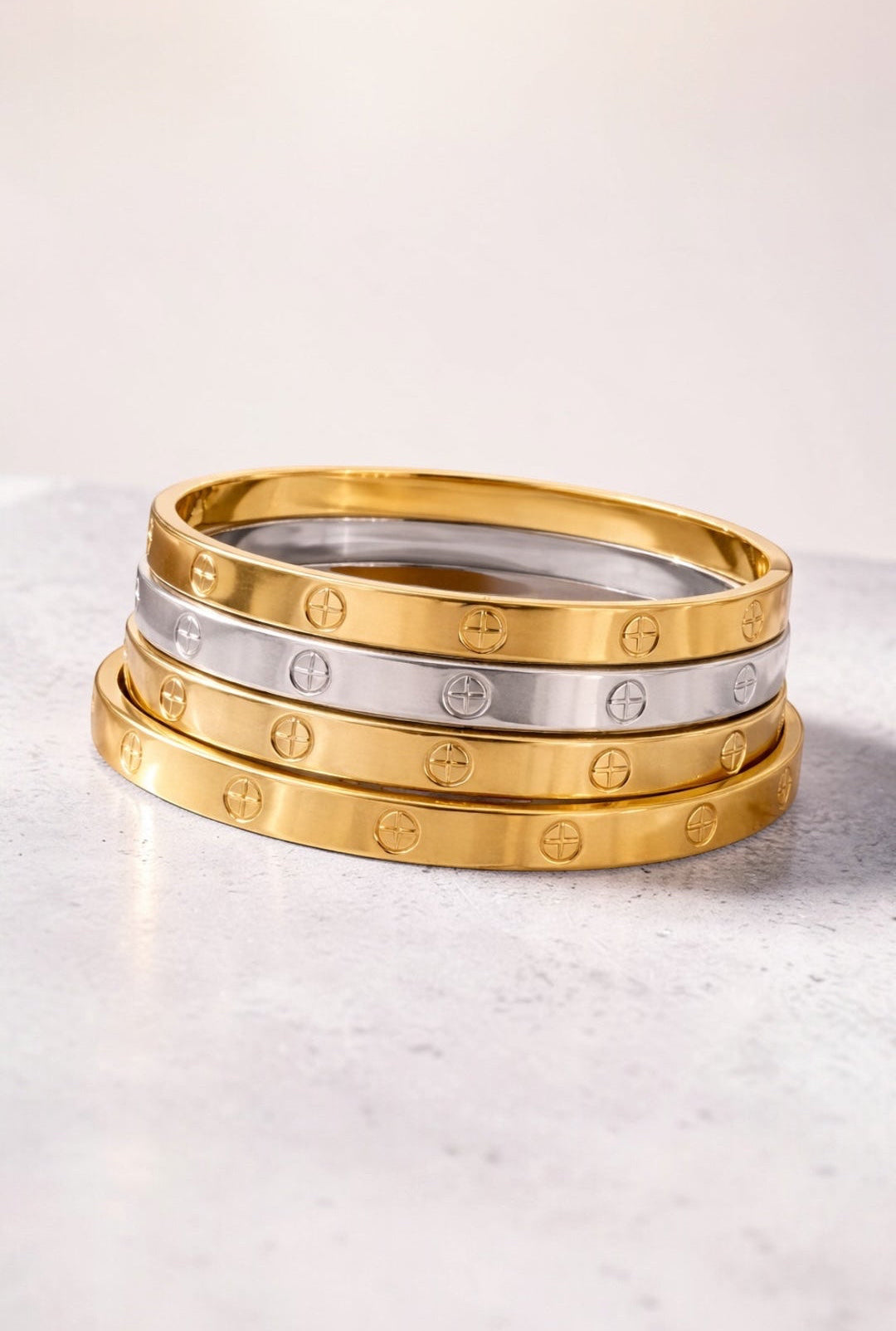 Three gold and silver bracelets stacked on a light surface